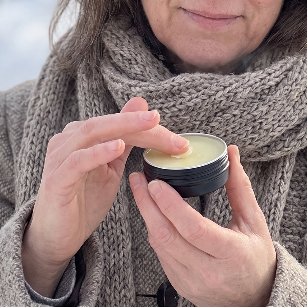 A woman on a winter day with a tin of Peppermint Beeswax Lip Balm